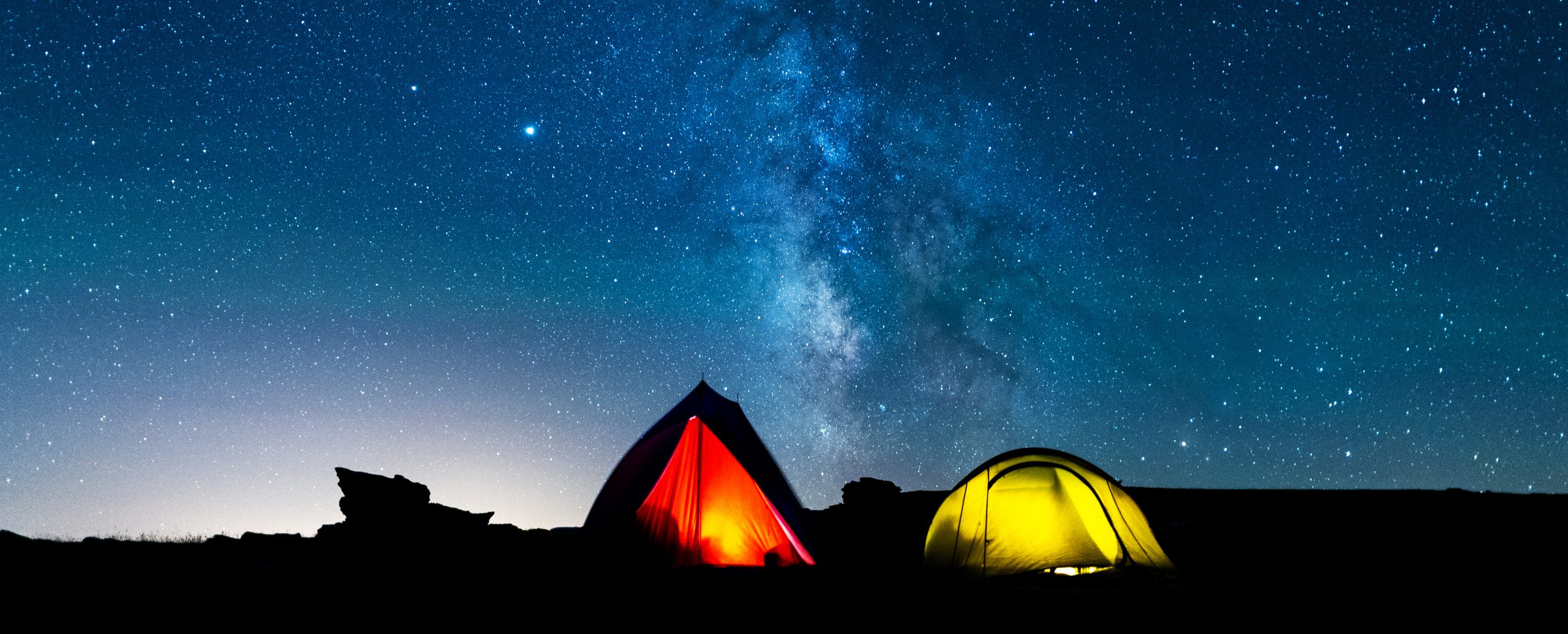 Tents glowing under the milky way at night. Camping in the mountains under the starry magical sky. Camping and wild life concept. Real outdoor adventure.